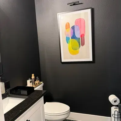Black painted accent wall in powder room with framed art and picture light — Plano, TX | Goldstar Renovations
